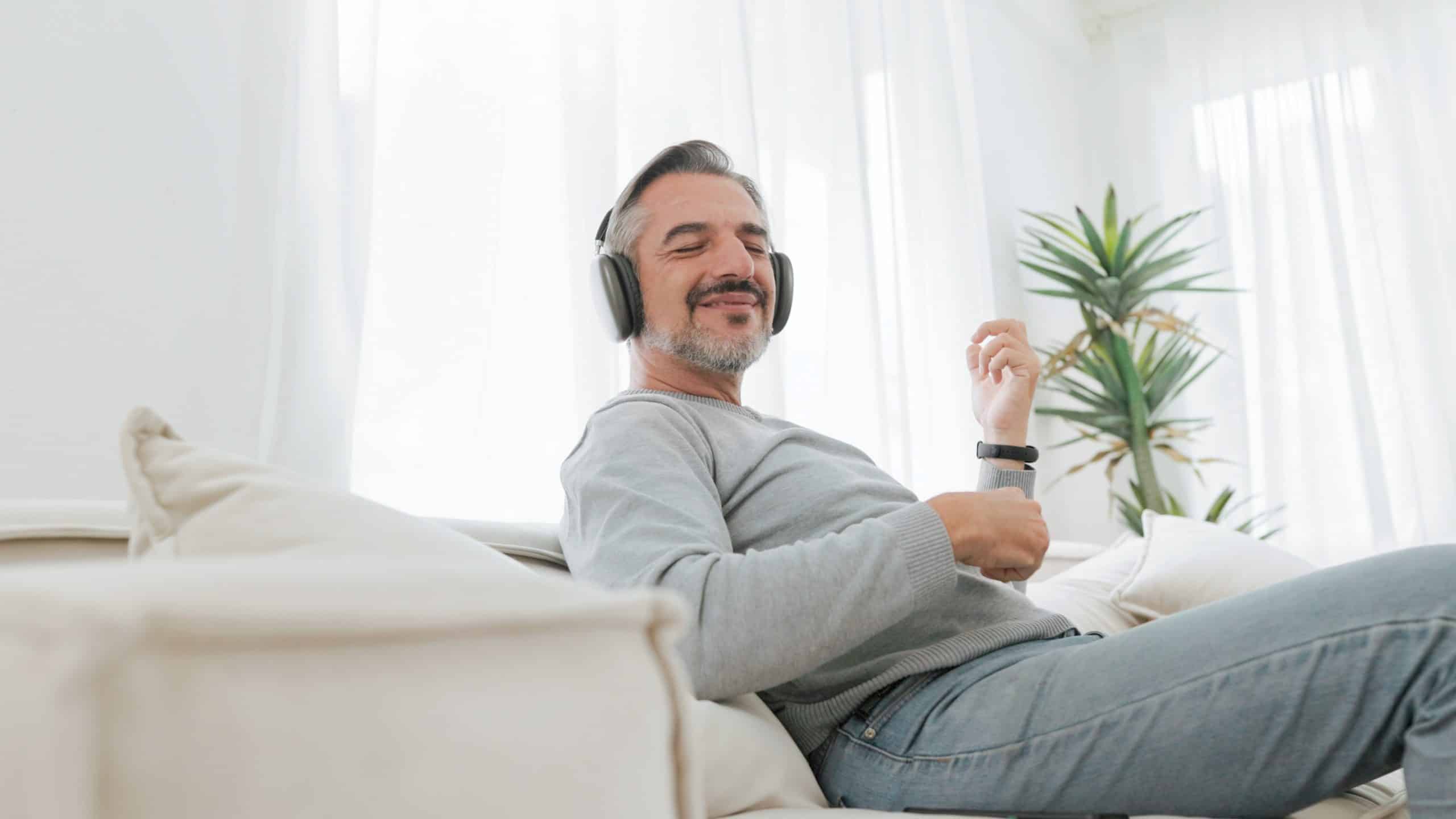 Senior Mature Adult Man Sitting On Sofa Listening To Music